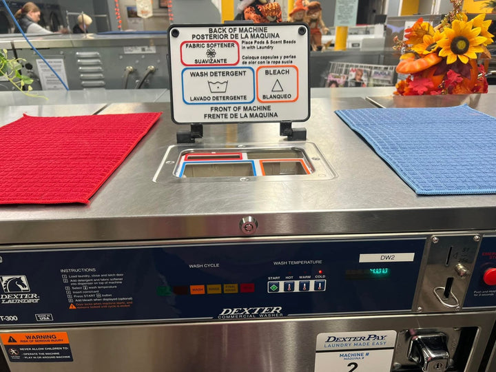 Dexter T-300 control panel in a laundromat with a DexterPay card reader, the top hopper open behind it with a labeled soap tray liner installed.