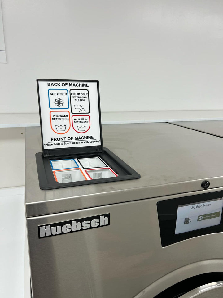 Top deck of a Huebsch Galaxy hardmount washer with the four-compartment supply hopper open and a color-coded liner and label installed.
