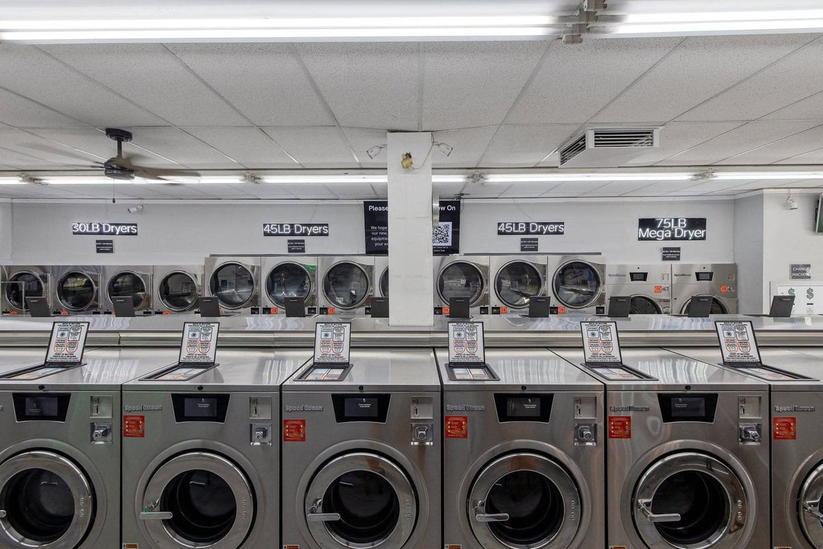 Straight-on row of Speed Queen Quantum Touch hardmount washers on a laundromat floor, touchscreen controls lit and doors closed.