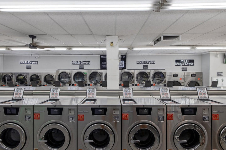 Straight-on row of Speed Queen Quantum Touch hardmount washers on a laundromat floor, touchscreen controls lit and doors closed.